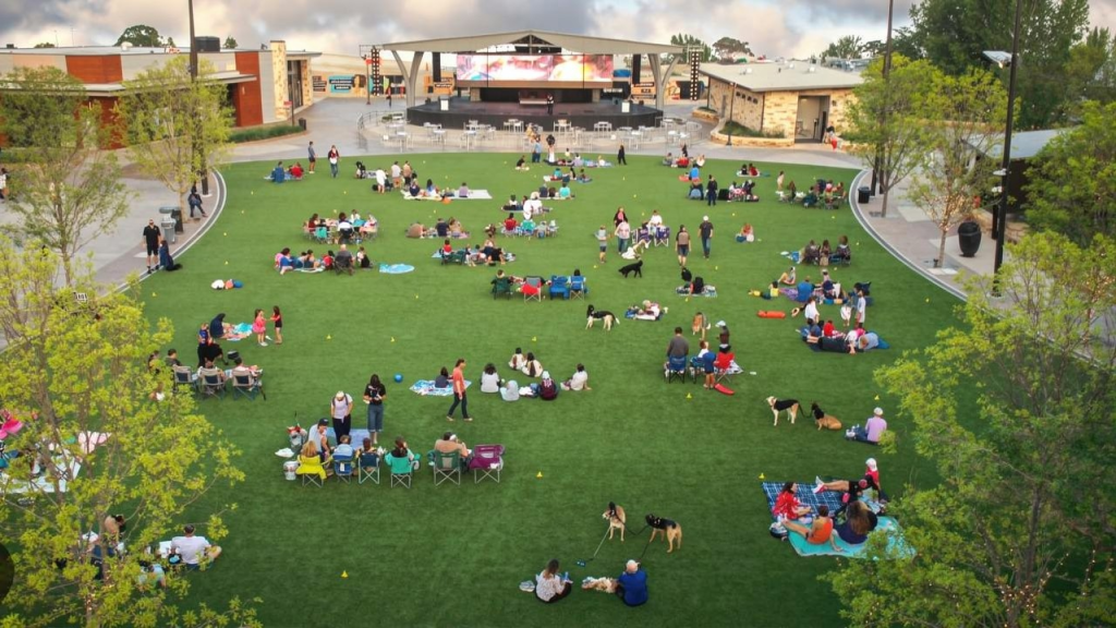 People sitting on grass watching a performance at Grandscape in The Colony Texas